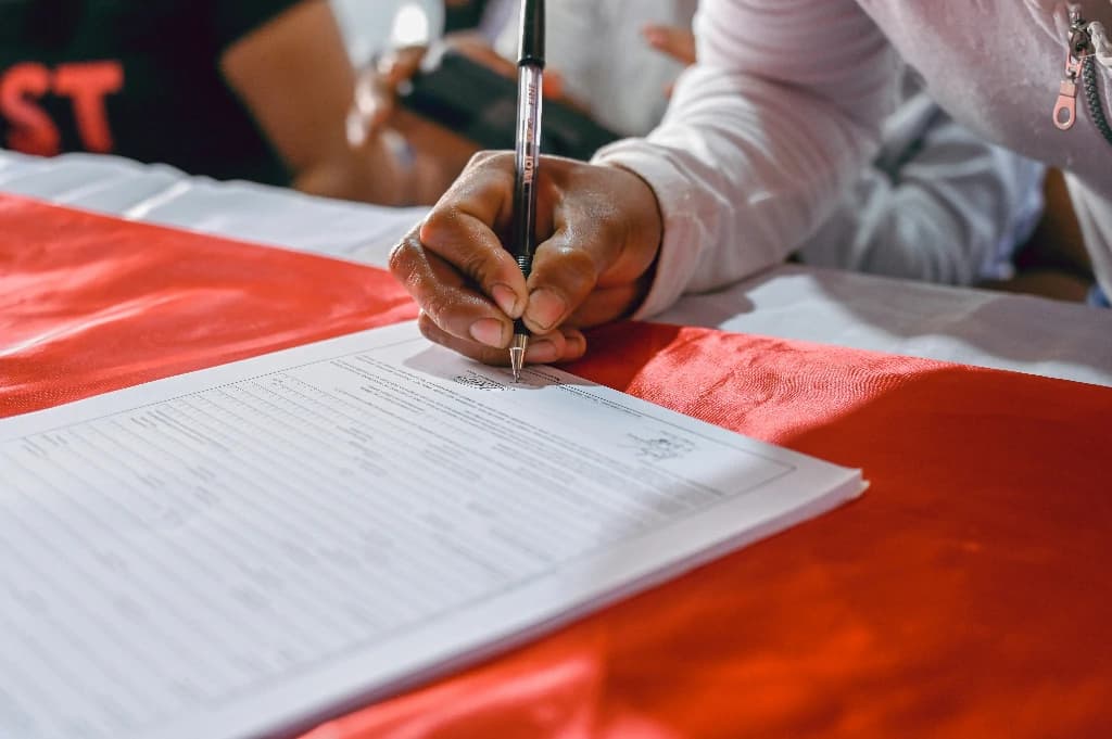 black female hand signing petition on a red table